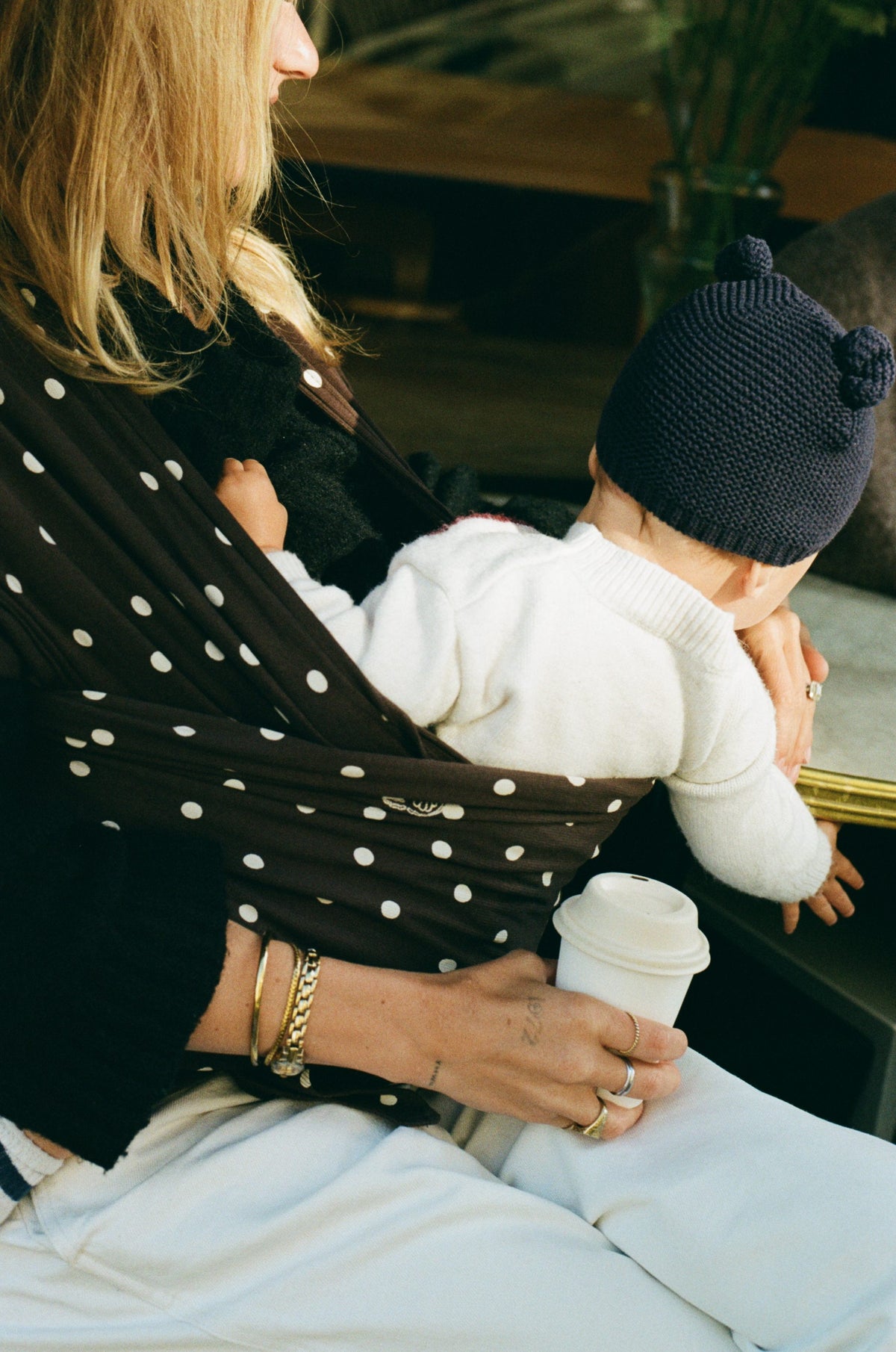 A mother feeding her baby a bottle, a Pierrot Dot Salomë muslin cloth over her shoulder.
